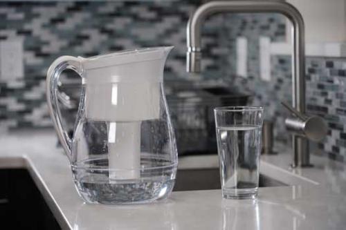 A water pitcher and a glass of water on a countertop