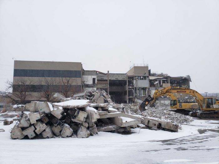 A building, half in rubble, under a layer of new snow and grey skies.