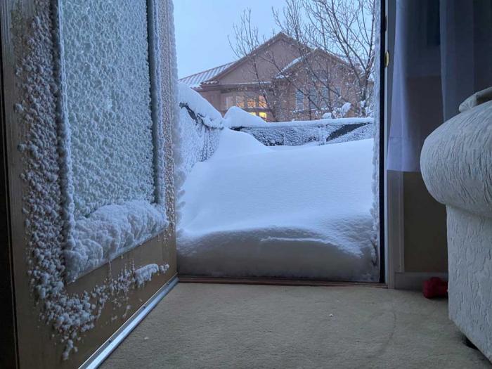 A snow-encrusted door opens onto a snow-covered patio, with another house seen in the distance.