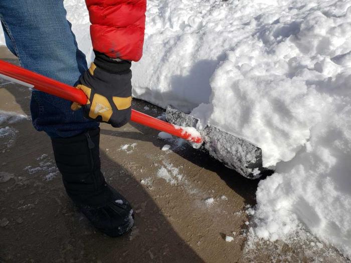 A shovel full of snow is lifted off the sidewalk.