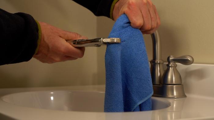 Hand using a towel and vice grip to remove faucet aerator