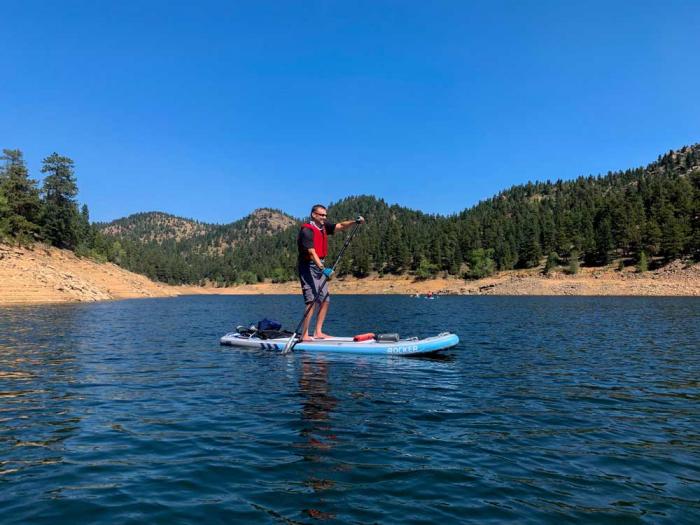 Man paddleboarding on a reservoir wearing a life jacket.