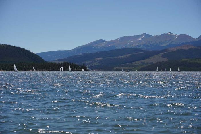 White sails on sailboats are visible in the distance on a reservoir, with mountains in the background.