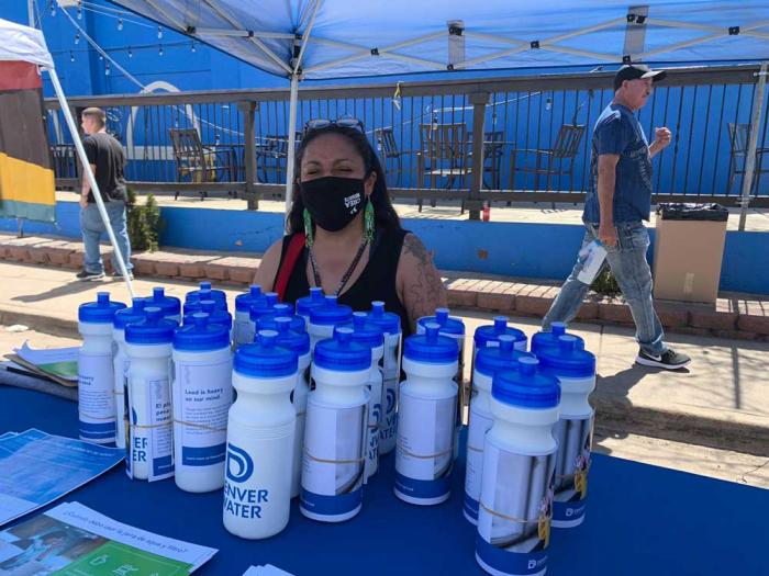 A woman in a mask to protect from COVID sits at a table with several Denver Water bottles with the utility's logo.