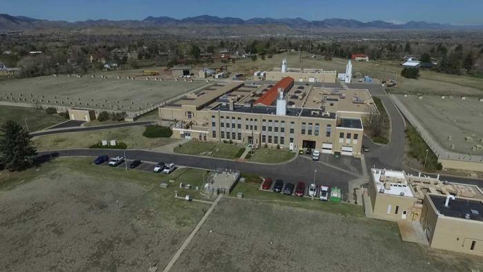 An aerial view of an old treatment plant building, surrounded by lawn with mountains in the distance.