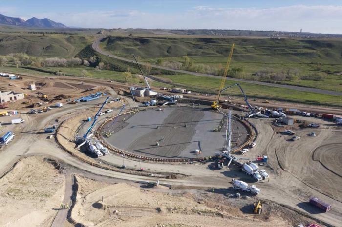 A view of the round base of the storage tank with Highway 93 rising into the green hills at the top of the picture.
