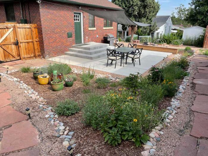 The same yard with a patio, green plants and smooth, round river stones around the edge.