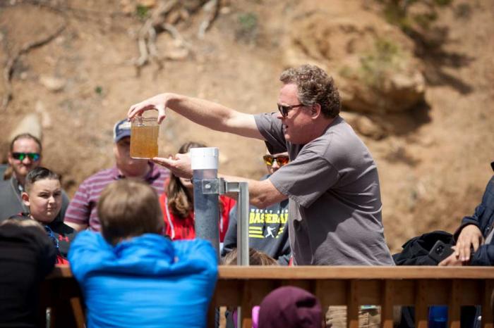 A man holds a beaker of dirty, brown water in front of a group of children.