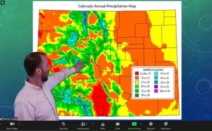 A man stands in front of a screen with a map of Colorado, marked in green, red and yellow for different rainfall levels.