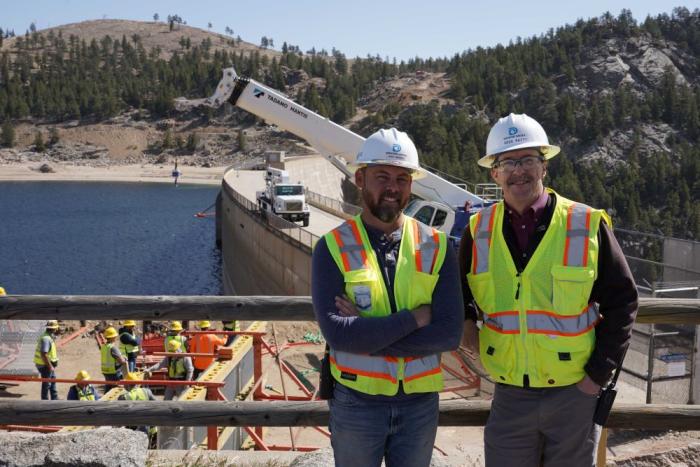 Two men stand near a dam