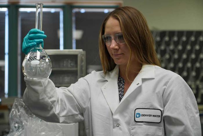 Woman in lab coat looking at a beaker of water.
