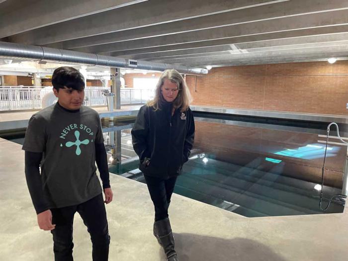 A man and a woman walk along the side of a pool filled with water inside a treatment plant.