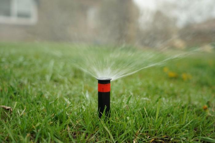 A sprinkler sprays water into the air on the front lawn of a home.
