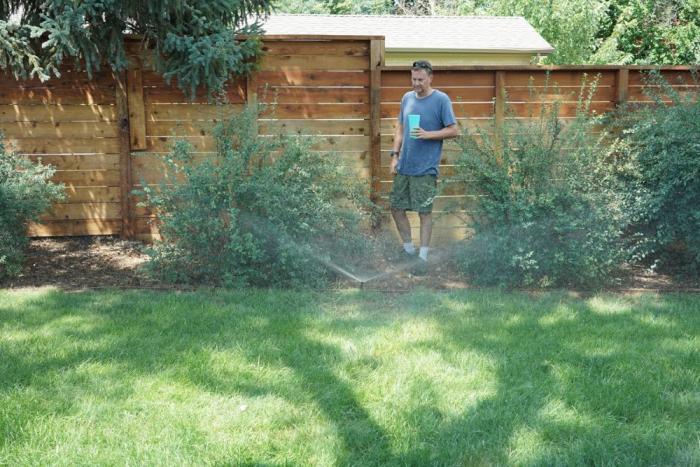 Man stands in lawn with sprinklers running