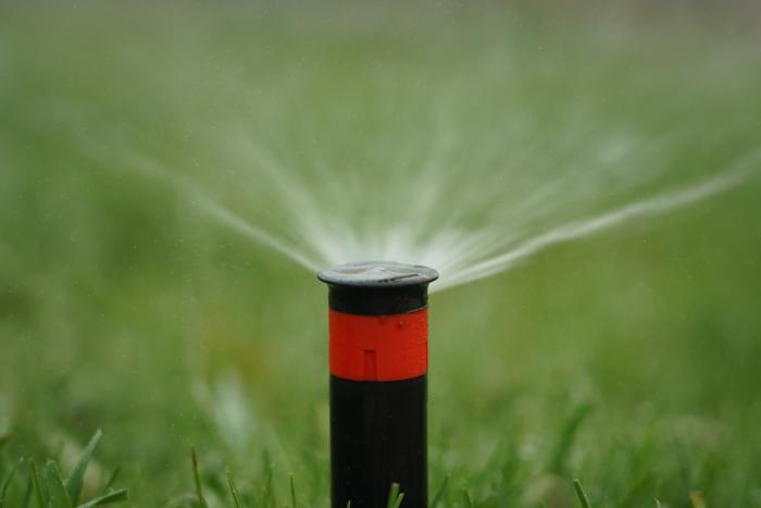 A sprinkler spraying water on a green lawn.