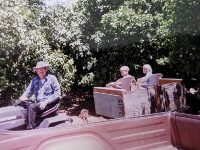 A boy and girl on a tractor with an older man driving it. 