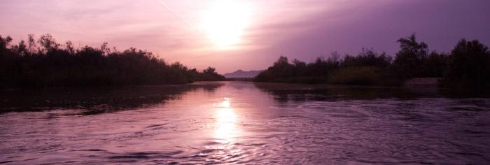 The sun sets over a river, with the light reflected in the water. 