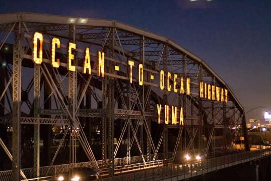 A bridge seen at night with words lit up saying "Ocean to Ocean Highway" and "Yuma." 