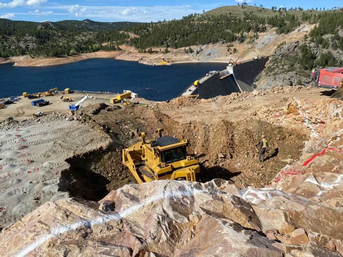 A bulldozer is in a hole with the reservoir in the background.