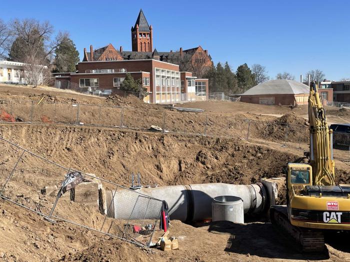 A construction site, with a pipe laying in the dirt and the Loretto Heights tower in the background.