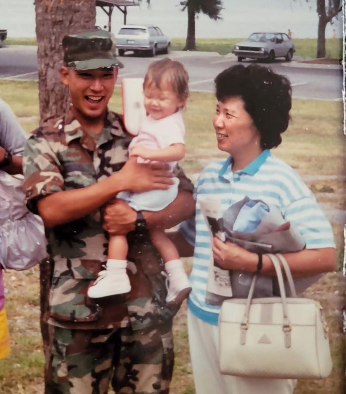 Man in uniform holds baby and stands next to a woman