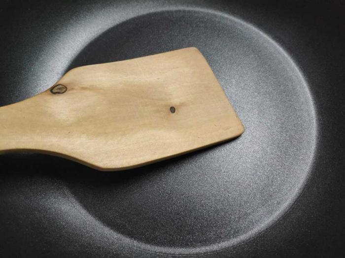A wood spatula scrapes the bottom of a nonstick pan.
