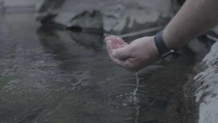 A hand dipping water out of a stream.