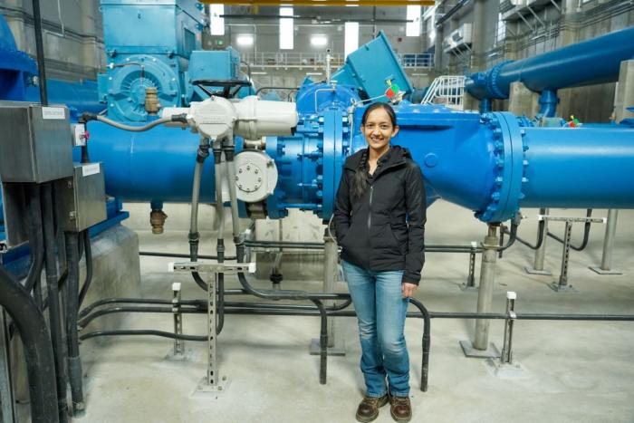 Woman stands in front of large blue pipes