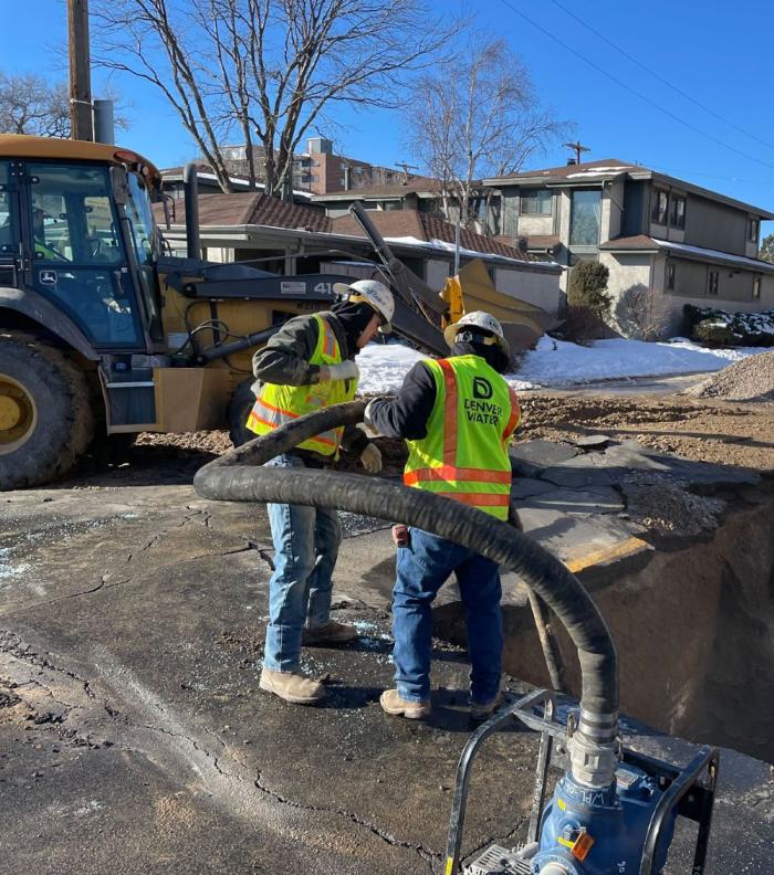 Two workers pump out water from a hole in the street