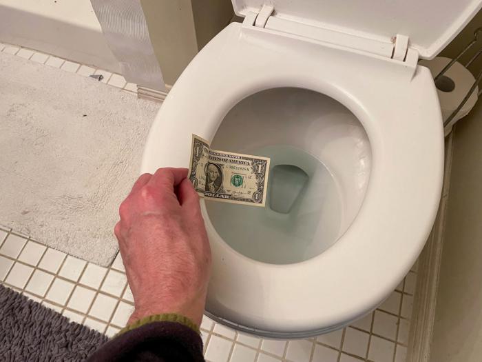 Hand holding a dollar bill over a toilet bowl.