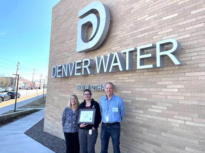 Three people hold an award in front of a Denver Water sign