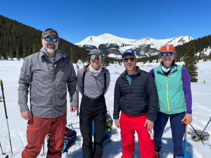 A group of four people stand in the snowy mountains