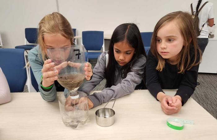 Three girls pour water through a filter