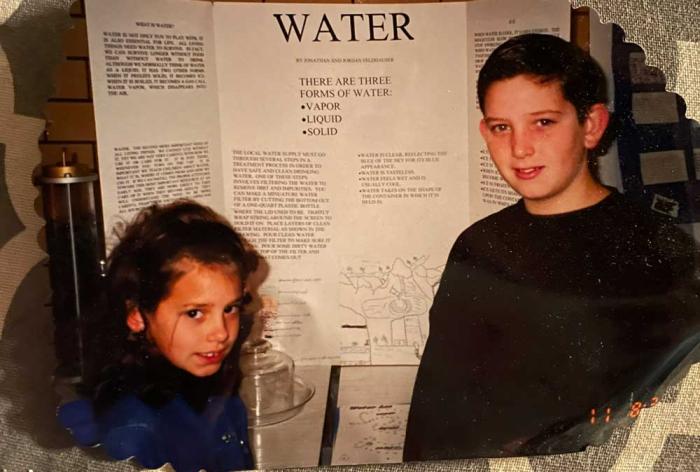 A boy and girl stand in front of a poster about water. 