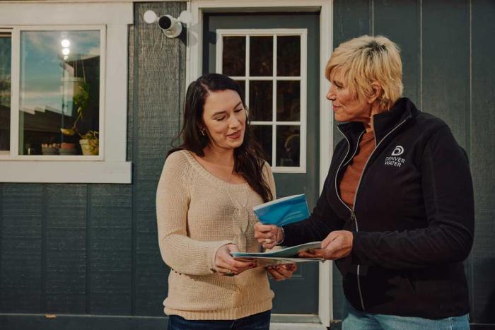 A woman, a homeowner, talks to a woman wearing a Denver Water fleece about information the two are looking at. 