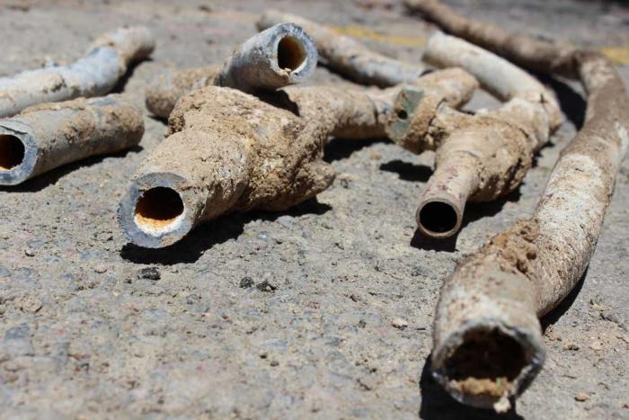 Lead pipes laying on a street, encrusted with dirt from being in the ground for decades.