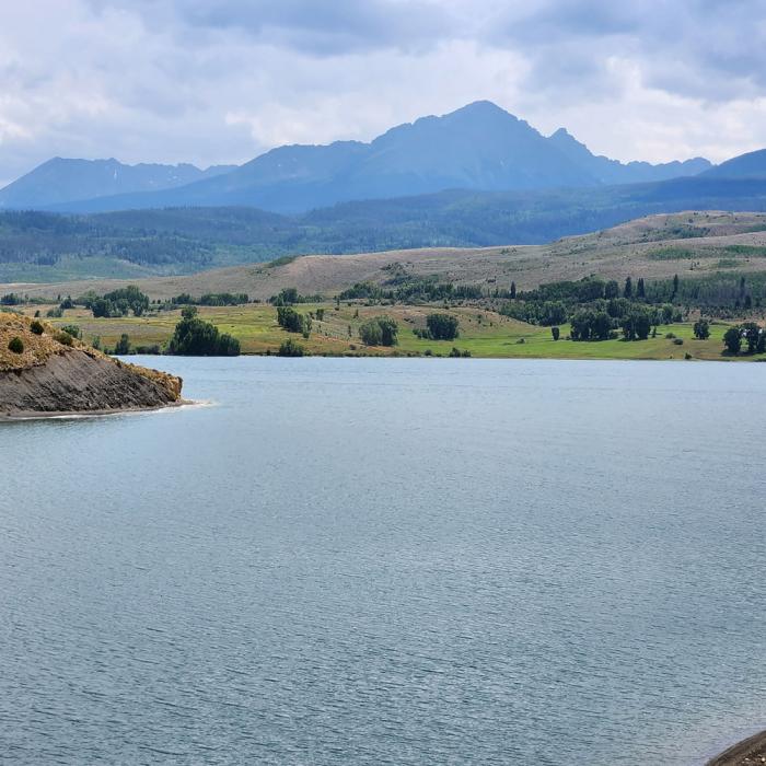 A large reservoir under cloudy skies with a huge range of mountains in the distance. 