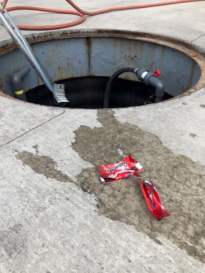 Plastic candy wrappers lie on the concrete next to a hole. The wrappers have been fished out of the water recycling units. 