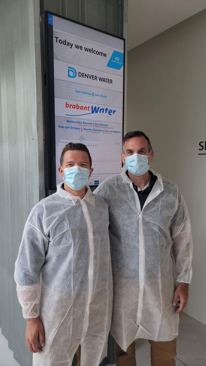 Two men wearing white safety masks and gowns. 