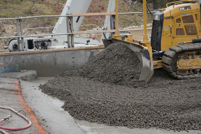 A bulldozer spreads pebble-type material across a platform. 