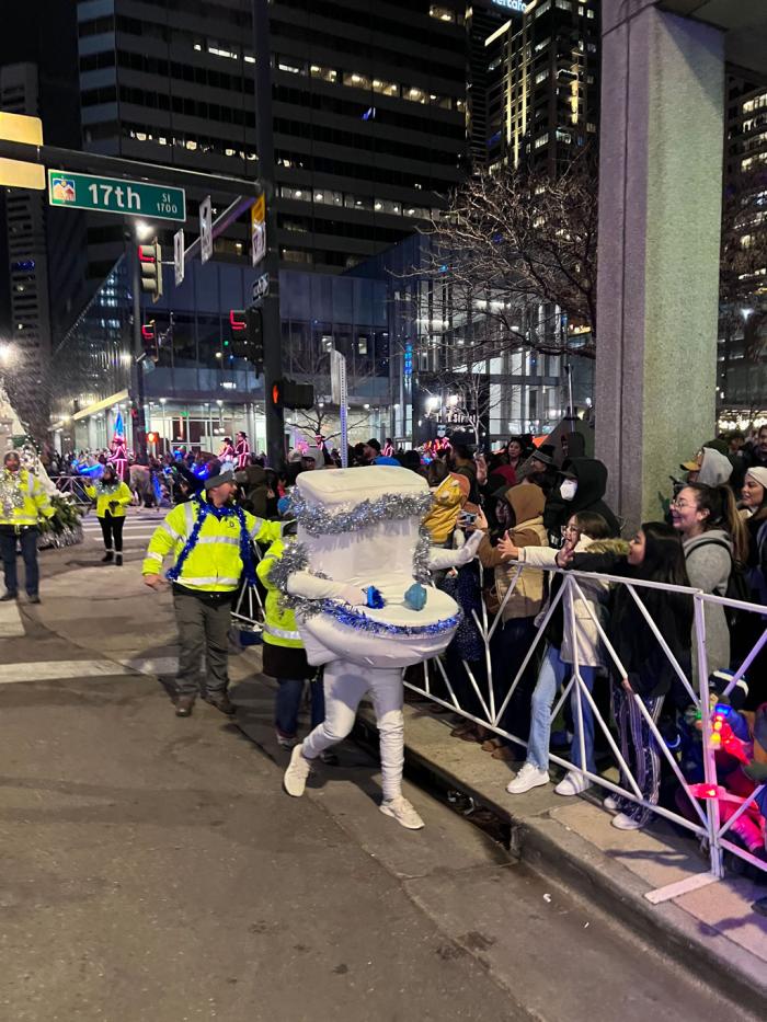 A person in a toilet costume runs along a barricade giving high fives to the people lining the parade route.
