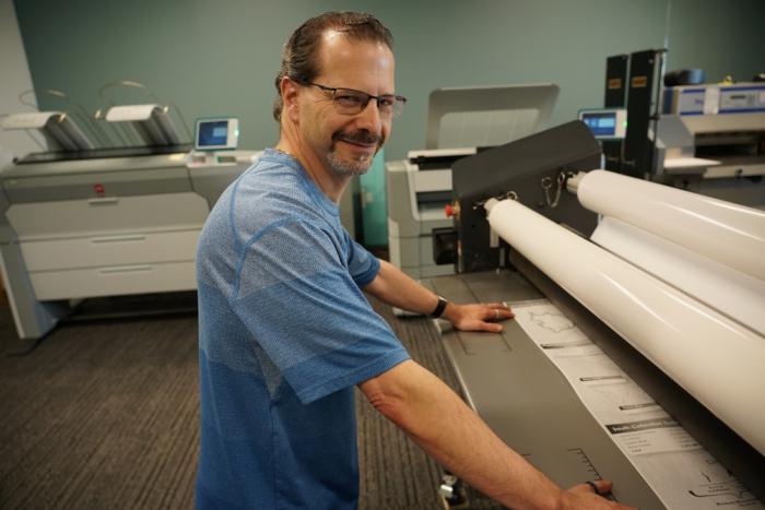 Man stands next to a large printer