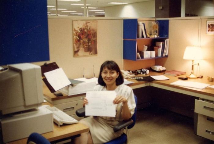 Woman sits at an office desk in the early 1990s