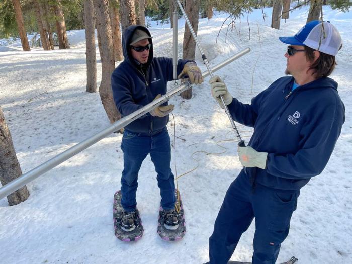 Two Denver Water workers have tubes in their hands as the stand in snow. 