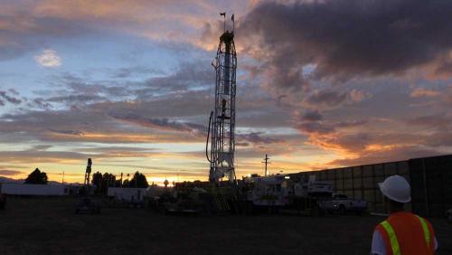 A drilling rig towers in the distance at dusk. 