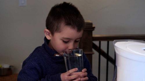 Child holds drinking water glass after he has poured water from lead reducing pitcher.