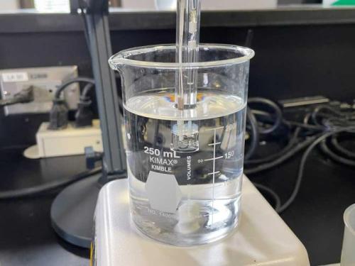 A 250 mL glass beaker filled with water has a sensor in it to measure the pH value of the water.