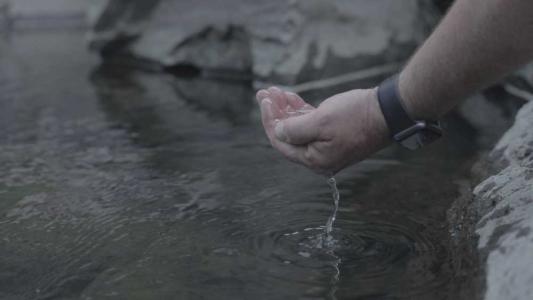 A hand dipping water out of the stream.