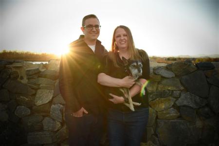 Two people hold a puppy while the sun sets behind them.