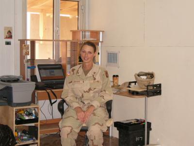 This photo shows a woman in military uniform sitting at a desk.